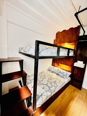 Een stapelbed met geometrische beddengoed, een houten bureau en een plank met opgevouwen handdoeken.