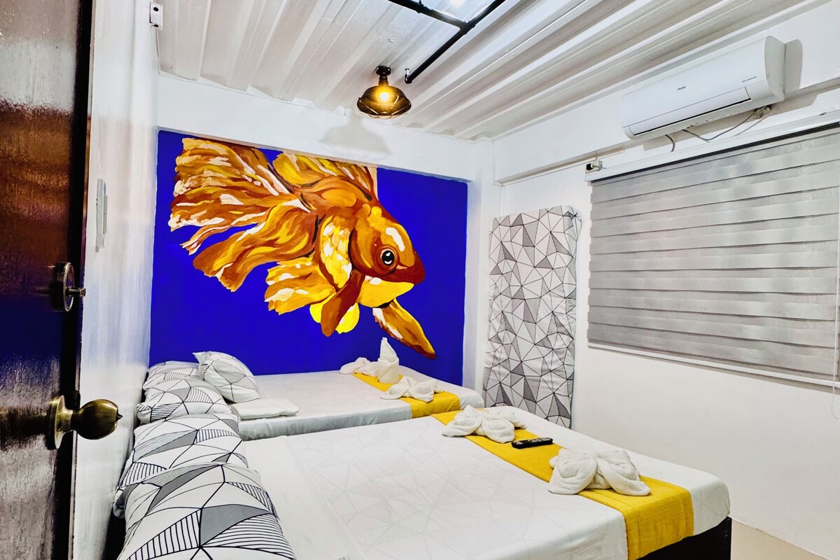 Ein Hotelzimmer mit einem Bett, einem Fischgemälde, einer Klimaanlage und einem Fenster mit Jalousien.