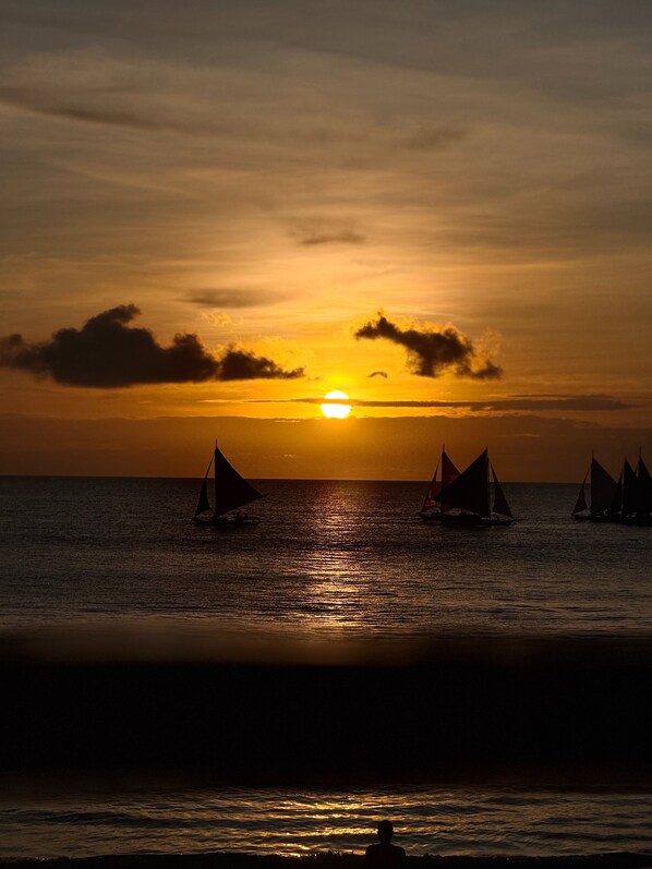 A sunset over the ocean with sailboats.