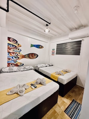 A hotel room with two beds, a ceiling fan, a painting of fish, a window with blinds, and a small rug.