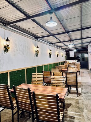 Un restaurante con mesas y sillas de madera, paredes verdes y faroles colgantes.