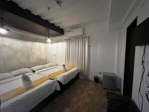 Une chambre d’hôtel avec deux lits, un ventilateur de plafond, un appareil de climatisation, une petite poubelle et un bureau avec un ordinateur.