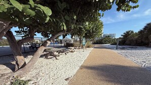 Zona de playa arenosa con mesas de picnic y un paseo pavimentado.