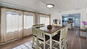 Un comedor con mesa y sillas de madera, una cocina al fondo y un techo con paneles de madera y una lámpara.