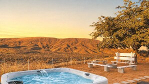 Uma banheira de hidromassagem com vista para uma paisagem montanhosa, rodeada por área de estar externa e uma árvore.