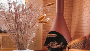 Ein gemütliches Wohnzimmer mit einer weißen Vase gefüllt mit Trockenpflanzen, einem Holztablett und einem Kamin mit Holzscheiten.