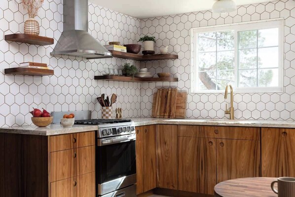 A kitchen with wooden cabinets, a stainless steel stove, and a window with a view of trees. - Flamingo Social Club • Boutique Luxury, Romantic Hot Tub with Fireplace (Yucca Valley)
