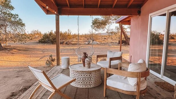 Eine Außenpatio mit Holztisch, zwei Lounge-Stühlen und einem runden Tisch mit einer Vase und Kerze.
