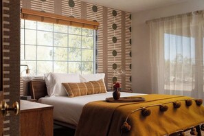 A bedroom with a large window, a bed with a yellow blanket, and a wall with a geometric pattern. - Flamingo Social Club • Boutique Luxury, Romantic Hot Tub with Fireplace (Yucca Valley)