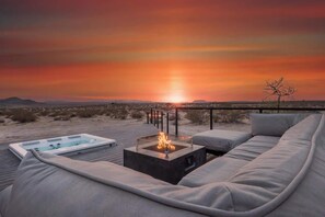 Vista al tramonto da un patio con un braciere, posti a sedere all'aperto e una piscina.