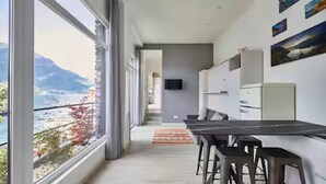 A modern kitchen with a long countertop, bar stools, and a view of the mountains through large windows. - Romantic studio with terrace overlooking the lake. (Lezzeno)
