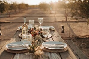 A wooden table set for a meal outdoors with plates, cutlery, and wine glasses. - Joshua Tree Olive Farm • Serenity, Spa, Views (Joshua Tree)