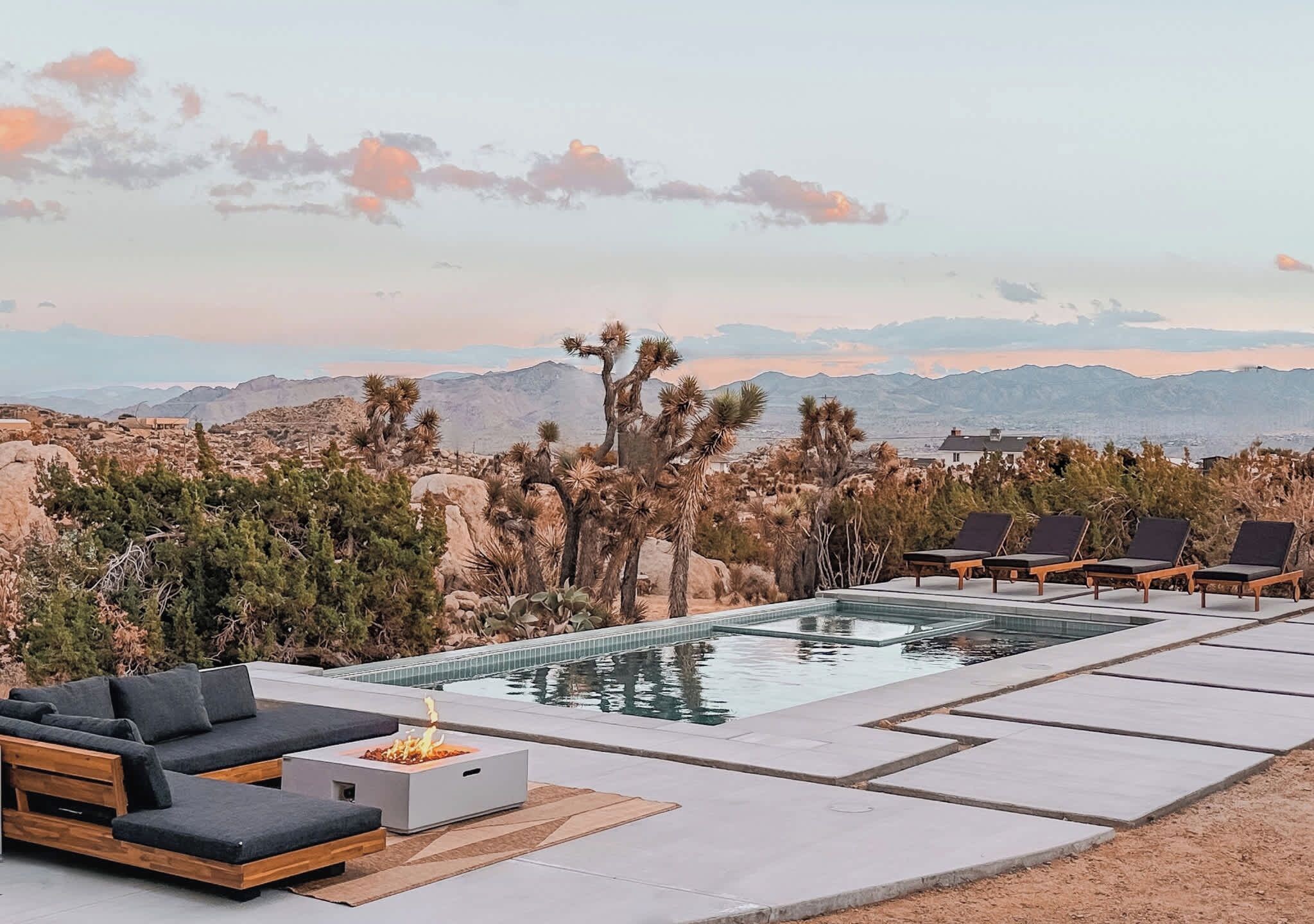 A pool area with lounge chairs and a fire feature, surrounded by desert vegetation and mountains in the background.