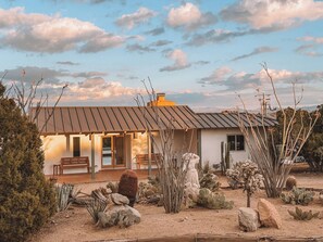 A desert-style building with a metal roof, a patio with a bench, and a cactus garden. - Looking Glass · Luxury Pool & Spa Villa (Yucca Valley)