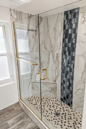 A modern shower enclosure with glass doors, marble walls, and a patterned floor. - Pipes Canyon Homestead · Hot Tub, Views, 5 Acres (Yucca Valley)