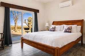 Un dormitorio con una cama grande, una mesita de noche, una lámpara y vistas a un paisaje desértico a través de un ventanal corredera.