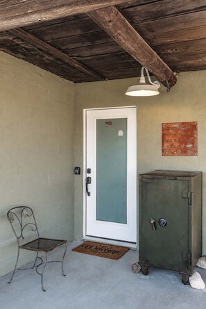 A room with a door, a metal chair, a metal cabinet, and a welcome mat. - Pipes Canyon Homestead • Privacy, Epic Views, Spa (Yucca Valley)