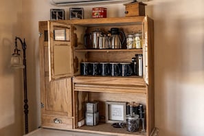 Un armario de madera con estantes que contiene equipo para preparar café, un bote de café y un cartel enmarcado.