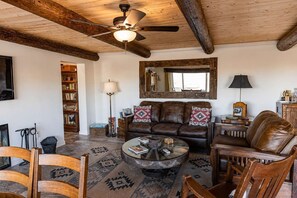 A cozy living room with a leather sofa, wooden chairs, a coffee table, and a ceiling fan. - Pipes Canyon Homestead • Privacy, Epic Views, Spa (Yucca Valley)