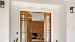 Una puerta de madera con paneles de vidrio que da a una habitación con chimenea y una silla.