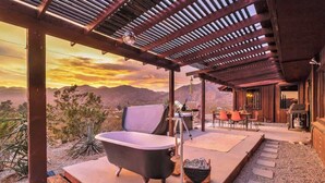 Un bagno esterno rustico con una vasca da bagno indipendente, un pergolato in legno e vista sulle montagne.