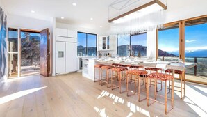 A modern kitchen with a large island, bar stools, and large windows offering a scenic view.