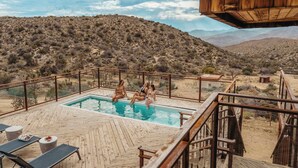 A pool area with a wooden deck, surrounded by desert landscape and mountains.