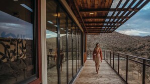 A wooden deck with glass railings overlooking a desert landscape.