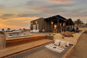 A modern outdoor spa area with a hot tub, lounge seating, and a wooden deck. - Shadow House · Walk to JT Park, Hot Tub, 10 Acres (Joshua Tree)