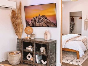 A bedroom with a bed, a bedside table, a wall-mounted TV, and a bookshelf. - Starlight Sanctuary • Romantic Stargazing Escape (Joshua Tree)