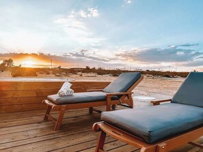 Deux fauteuils confortables sur une terrasse en bois, avec vue sur le coucher de soleil.