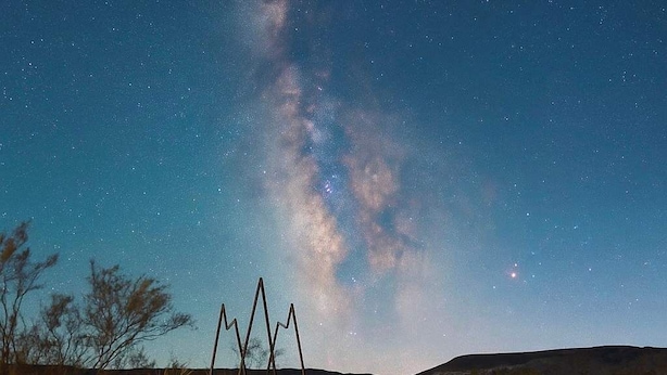 Una persona in una vasca idromassaggio sotto un cielo stellato con una chiara Via Lattea.
