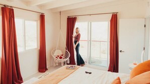 Una camera da letto con un letto, una sedia a dondolo e vista sull'esterno attraverso ampie finestre.