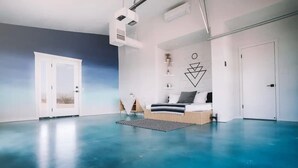 A modern room with a blue floor, a bed with a white headboard, a small desk, and a wall-mounted shelf with decorative items. - Starship Landing • 2 Epic Houses Retreat, 10 Acres (Yucca Valley)