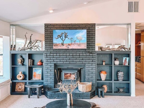 Een moderne woonkamer met een open haard, inbouwplanken met decoratieve objecten en een groot raam.
