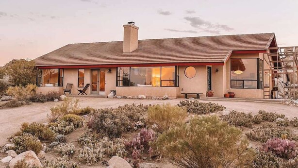 A modern house with a flat roof, large windows, and a patio area with outdoor seating. - Stone&Sky • Pool & Spa in Boulders (Yucca Valley)