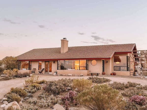 Una casa moderna con techo plano, ventanas amplias y un patio con mobiliario exterior.