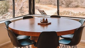 A dining area with a large round table, six chairs, and a hanging pendant light. - Stone&Sky • Pool & Spa in Boulders (Yucca Valley)