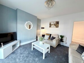 A living room with a flat-screen TV, a white coffee table, a beige sofa, and a floor lamp. - Toast Stays - The Stray Space (Darlington)