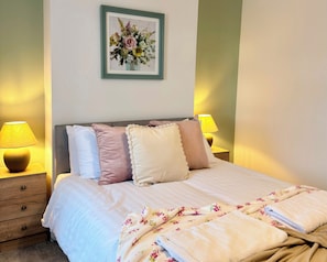 A neatly made bed with a floral-patterned blanket, a bedside lamp, and a framed floral artwork on the wall. - Toast Stays - The Stray Space (Darlington)