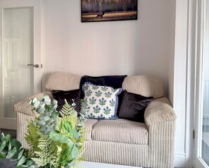 A beige sofa with a patterned pillow, a dark throw, and a small plant in a corner. - Toast Stays - The Stray Space (Darlington)