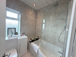 A modern bathroom with a glass-enclosed shower, a white sink with a countertop, and a window with decorative curtains. - Toast Stays - The Stray Space (Darlington)