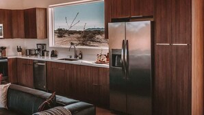 A modern kitchen with wooden cabinets, stainless steel appliances, and a large window with a desert view. - The Refuge • Healing Retreat, Saltwater Pool & Spa (Joshua Tree)