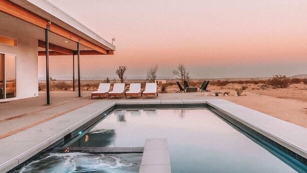 A modern outdoor pool area with lounge chairs and a desert landscape in the background. - The Refuge • Healing Retreat, Saltwater Pool & Spa (Joshua Tree)