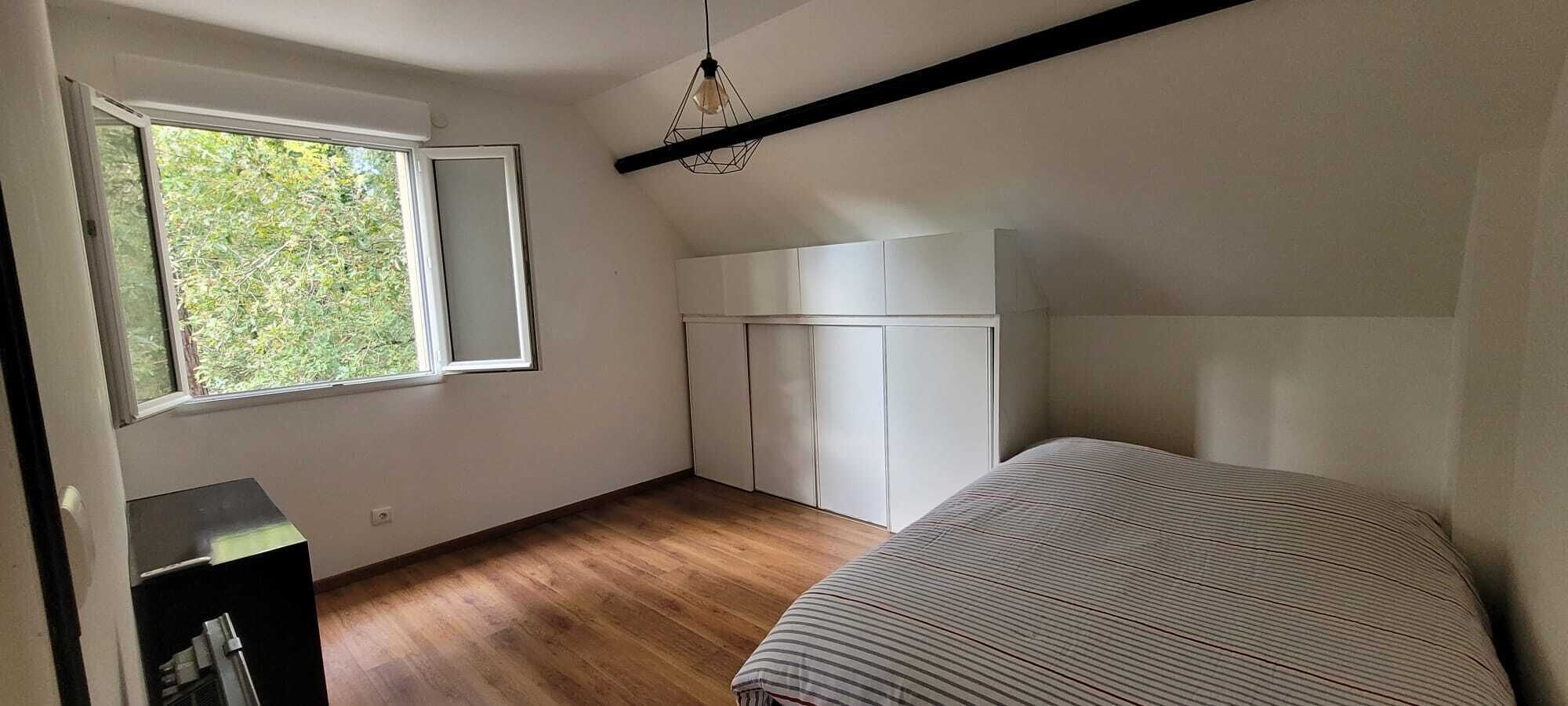 Un dormitorio con cama, armario, escritorio y ventana con vistas a la vegetación.