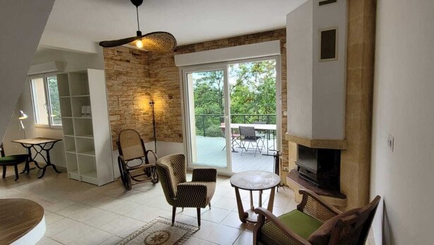 A modern living room with a fireplace, a dining area with a table and chairs, and a balcony with outdoor furniture. - Maison nichée au cœur de la nature, dans le parc naturel régional du gâtinais. (Nanteau-sur-Essonne)