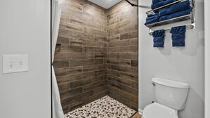 A shower with a tiled floor, a wooden wall, and a toilet with a white lid.