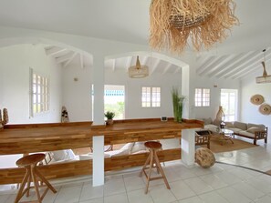 A spacious room with a high ceiling, wooden benches, a sofa, and a hanging light fixture. - Villa Caméo • Grande villa familiale vue mer 180° (Le Gosier)