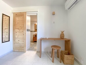 Une pièce avec un bureau en bois, un tabouret, un panier en osier et un tableau encadré accroché au mur.