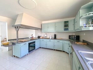A modern kitchen with light blue cabinets, a built-in oven, and a stainless steel range hood. - Villa Caméo • Grande villa familiale vue mer 180° (Le Gosier)